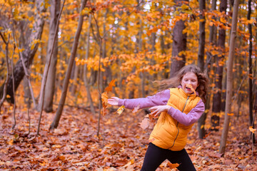 Full of joy and fun photo of a girl playing with autumn leaves in the forest.Shallow depth of field