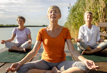 Fototapeta na wymiar Group of senior woman doing yoga exercises by the lake.