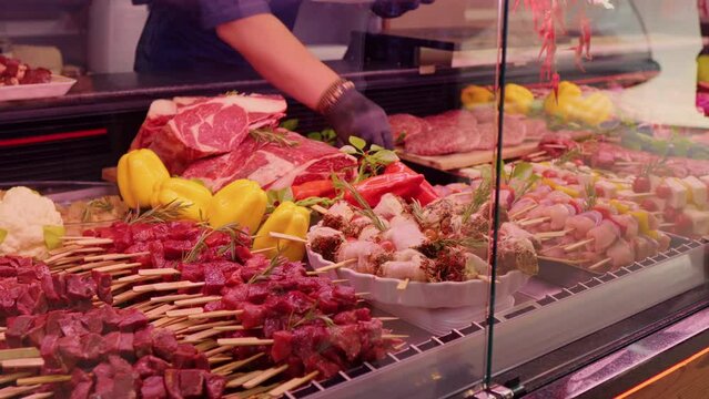 Mens hands picking chicken barbecue on skewers to be weighted. Window shop with different meat goods in butchers store.
