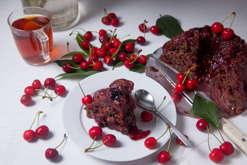 Chocolate cake with sweet cherry, cup of tea and bouquet of blue flowers on white background..
