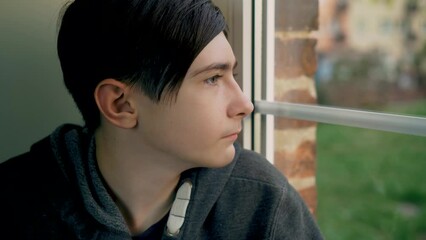 Portrait of boy teenager looks sadly at his reflection in window during curfew because russian armored invasion into Ukraine. Save lifes, no war, world peace, stop conflict, born love. Childhood in