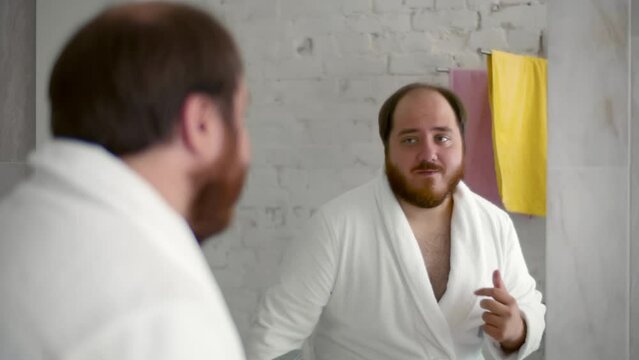 Happy man in bathrobe dancing shirtless in looking in mirror having fun. Realtime