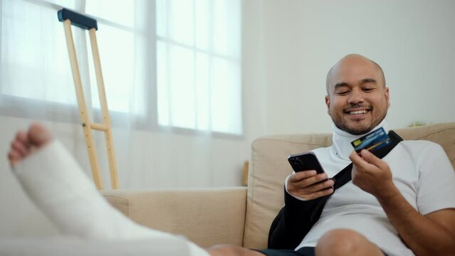 Happy man using credit card pay medical expenses from accident fracture broken bone injury with leg splints in cast, neck splints collar, sling support arm. Social security and health insurance.