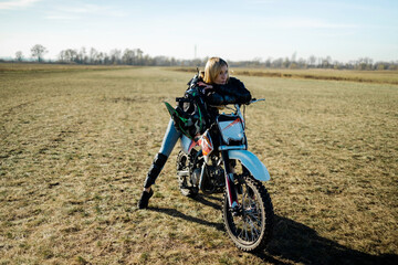 Fototapeta na wymiar Beautiful blonde woman in motorcycle outfit. Happy female sitting on her motorcycle.