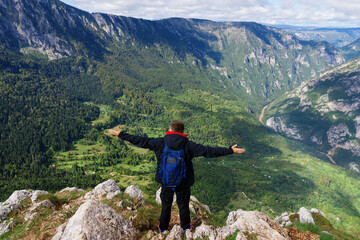 Top view of a tourist who stands on a cliff and looks at the mountain landscape