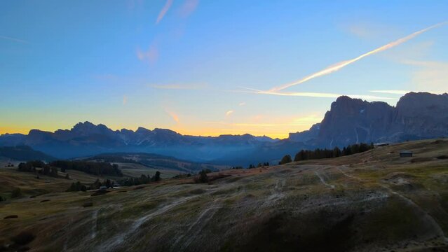 Mountains, forest and grass fields with wooden cabins filmed at Alpe di Siusi in Alps, Italian Dolomites filmed in vibrant colors at sunrise. Filmed with a drone with forward movement, wide view