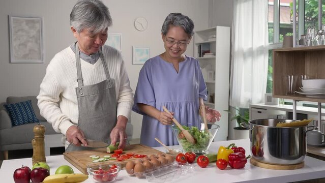 Happy Asian senior couple preparing food in the kitchen. Retired people cooking meal at home.