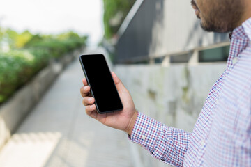 Closeup male hands using smartphone with blank copy space screen at city shopping street. Cropped shot view of man's hands holding smart phone searching or social networks during in urban setting.