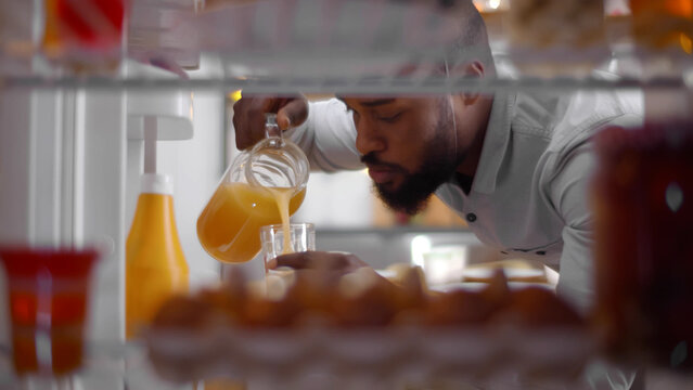 View from inside fridge of African-American man opening door and pouring glass of cool orange juice - Powered by Adobe