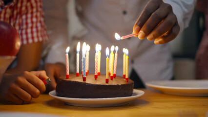 Close up of hands with candles lightening birthday candles on tasty cake. - obrazy, fototapety, plakaty