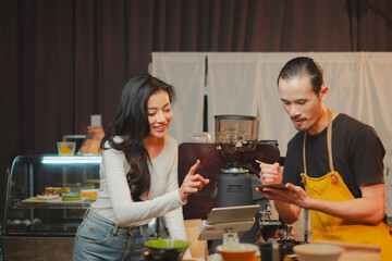 Male barista talking receive orders from customer at bar counter in coffee shop by digital tablet or kiosk. Female customer is ordering by a touch screen menu. Technology service.