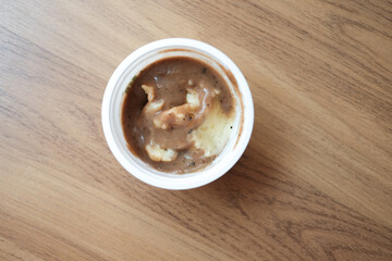 mashed potatoes with gravy sauce in a white cup plastic on wooden background.