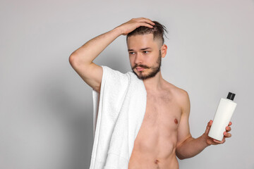 Fototapeta premium Naked man with towel and bottle of shampoo on light grey background