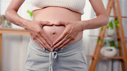 4k, Close Up The belly of a pregnant mother who is about to give birth with both hands forming a heart in the middle of her belly. Teenage mother stood in living room of house and rubbed stomach - Powered by Adobe