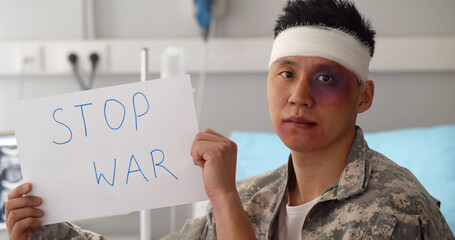 Injured asian soldier sitting in hospital ward and holding stop ward sign