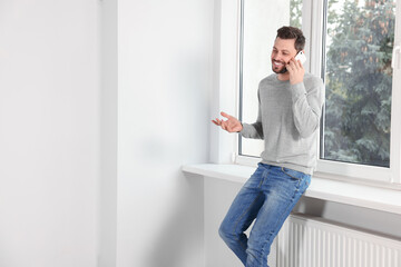 Fototapeta na wymiar Man talking on phone near window indoors, space for text