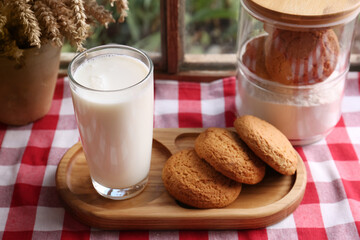 Glass of milk with cookies on red checkered tablecloth indoors