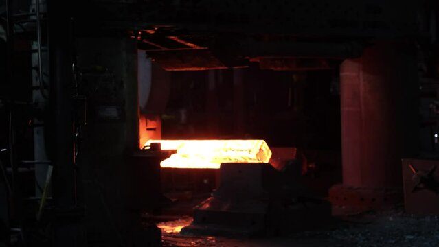 Blacksmith factory. Close-up of robots work. Forging a large hot metal billet with an industrial forging press. Technical equipment of a metal forging plant. Large machines, blacksmiths move and heat