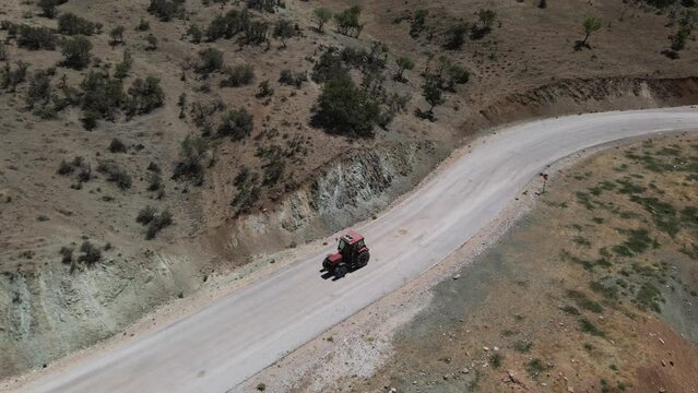 Drone following red trucktor slowly driving a road in turkey karaman between fields and mountains at a sunny summer