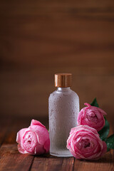 Bottle of essential rose oil and roses on wooden table. Space for text