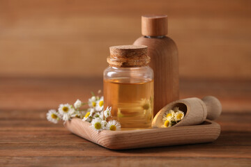 Bottles of chamomile essential oil and flowers on wooden table