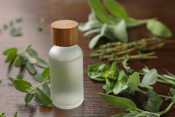 Bottle of essential oil and fresh herbs on wooden table