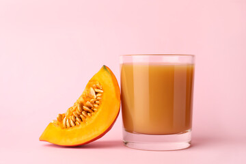 Tasty pumpkin juice in glass and cut pumpkin on pink background