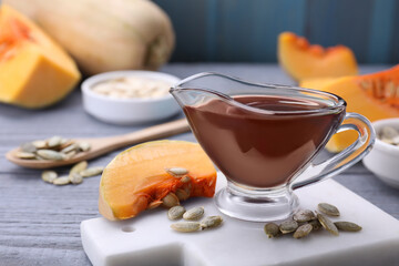 Fresh pumpkin seed oil in glass sauceboat on grey wooden table