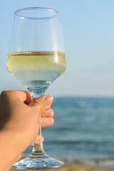 Woman holding glass of tasty wine near sea, closeup. Space for text