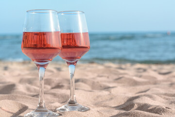 Glasses of tasty rose wine on sand near sea, space for text