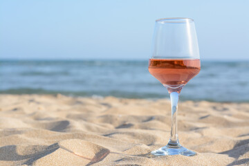 Glass of tasty rose wine on sand near sea, space for text