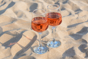 Glasses of tasty rose wine on sand