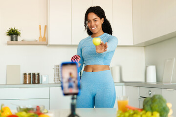 Healthy food blog concept. Happy african american woman recording video for her blog on smartphone, standing in kitchen