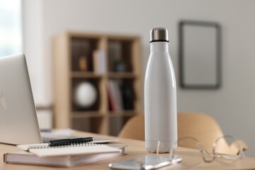 White thermos bottle on wooden table indoors. Space for text