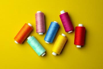 Different colorful sewing threads on yellow background, flat lay