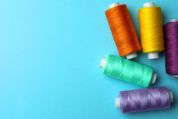 Different colorful sewing threads on light blue background, flat lay. Space for text