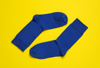Pair of new blue socks on yellow background, flat lay