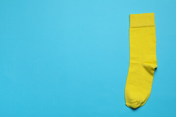 New yellow sock on light blue background, top view. Space for text