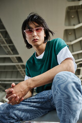 Vertical portrait of street style Asian man looking at camera outdoors and wearing pink sunglasses
