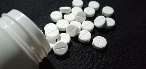 White medical pills scattered on a black background