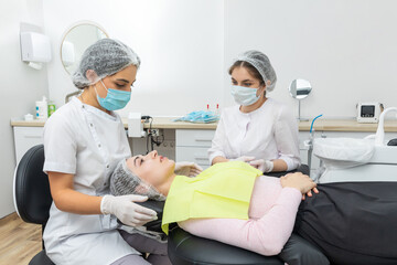 Dentist and assistant performing dental treatment inmodern dental clinic, patient laying in a chair