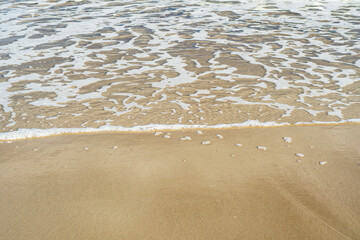 Fototapeta na wymiar Close-up of a sandy beach with a transparent wave. Sea coast on a summer day.