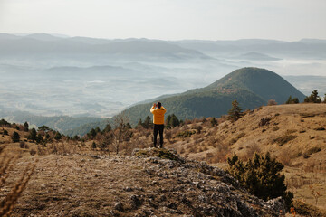 Fototapeta premium Man in a yellow jacket sitting on the rock among the mountains at sunny day in the forest in Turkey Bolu. Hiking concept