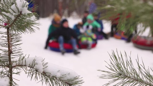 Funny children ride downhill in winter in turn in defocus. Cheerful friends, holidays, winter fun, snow-covered mountain slopes. Video, footage for the background, intro, titles. UHD 4K.