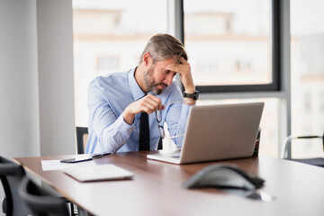 Shot of stressed businessman working with laptop at office