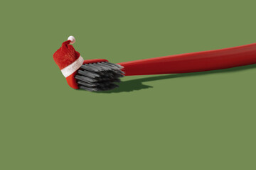 Single red toothbrush with red and white Santa hat laying on green background with copy space and shadow. Dental medical Christmas and New Year concept. Creative health still life levitation.