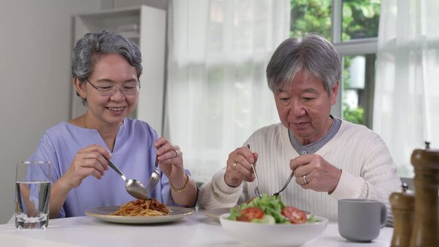 Happy Asian senior couple eating meal together in kitchen at home. Retirement senior couple lifestyle living concept.