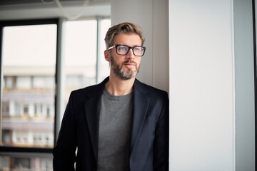 Portait of executive businessman deep in thought while standing at the office - 546266606