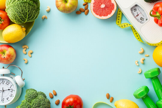 Proper nutrition concept. Top view photo of scales vegetables fruits nuts alarm clock dumbbells and tape measure on isolated pastel blue background with empty space in the middle