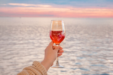 a glass of pink cider on the background of the water surface and the sunset sky